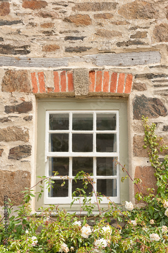 Old square wooden window in an old stone cottage wall with garden plants underneath