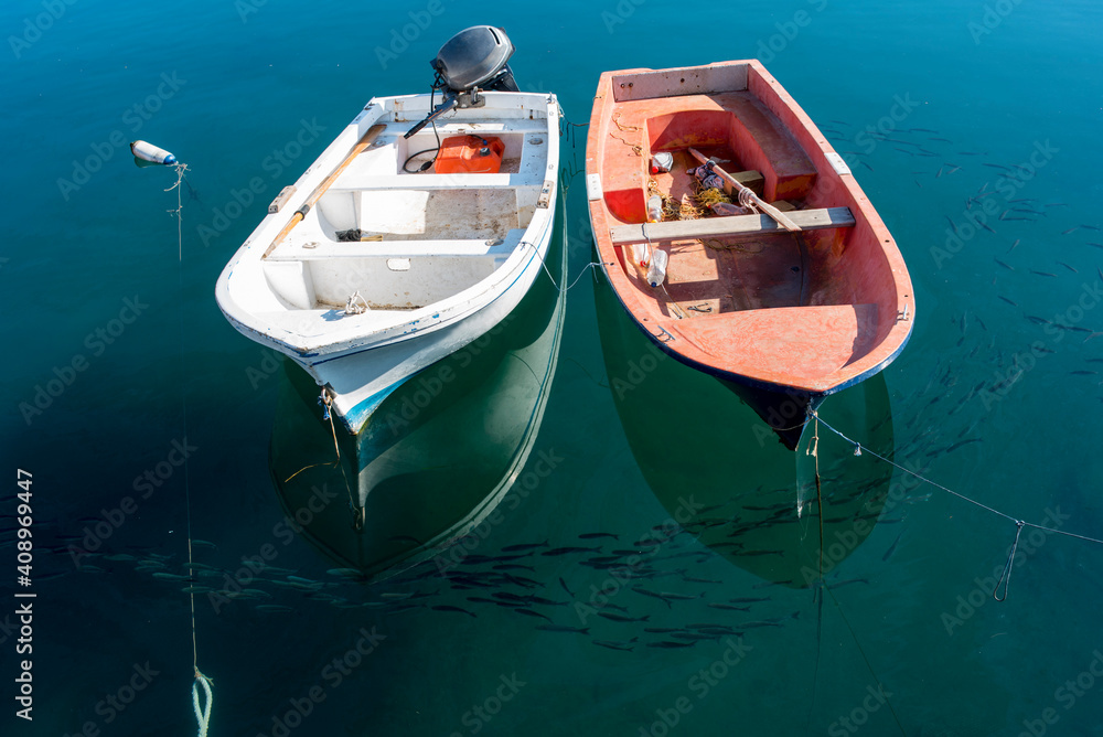 A white and a red boat moored together next to the shore of the beach