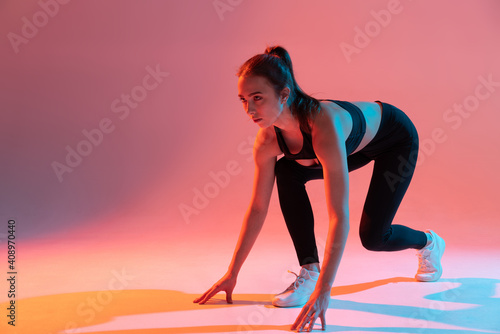 Athletic woman from starting position, ready to run. Multicolor light.