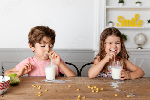 Happy siblings blowing milk bubbles at kitchen table