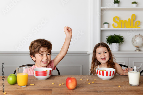 Happy siblings eating cereals at kitchen table