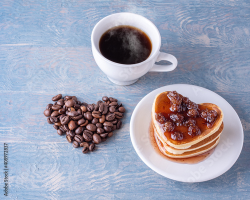 Breakfast for a lover. Homemade heart shaped pancakes with berry jam  heart shape made from coffee beans  white cup of hot coffee on a blue wooden table
