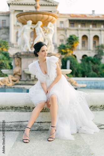 Portrait of Beautiful bride in white fashion wedding dress. Outdoor romantic portrait of attractive brunette woman with hairstyle posing by fountain at park.