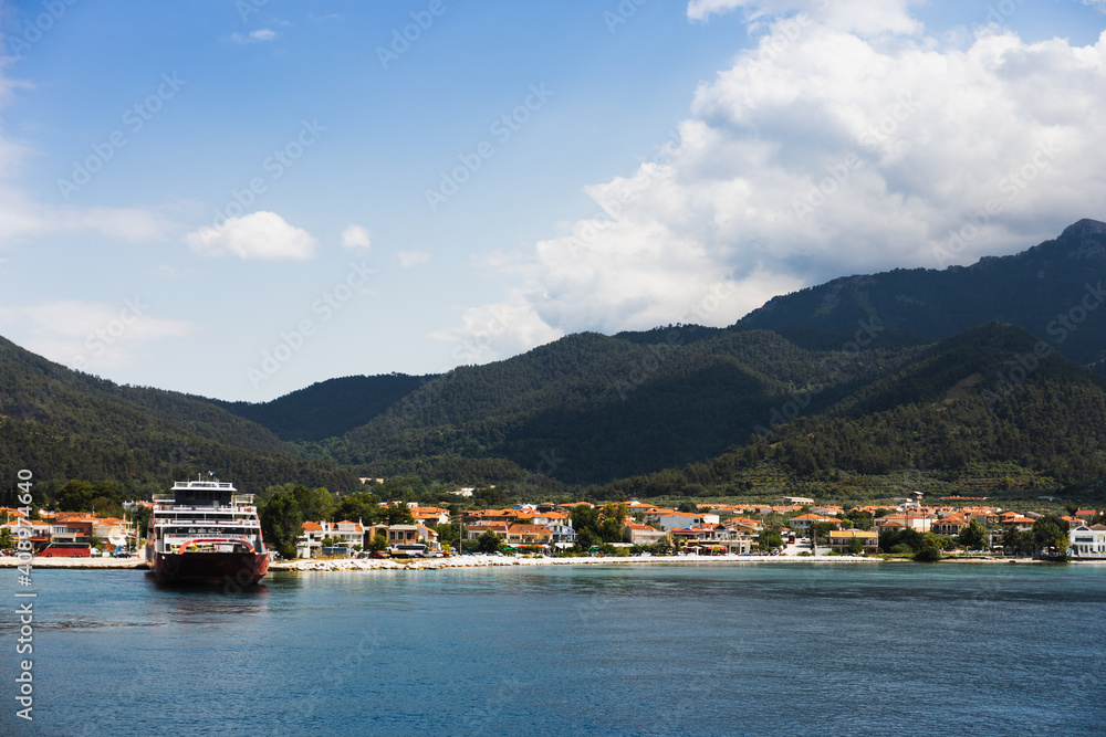 tourist summer landscape in greece, island, port, ferry, city, beach, mountains with forest, sea with turquoise and blue water, blue sky with clouds
