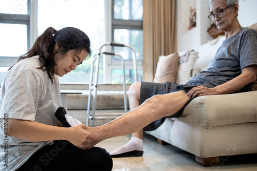 Asian daughter taking care of helping elderly,woman wear socks on feet of her senior mother,old people with cold toes,numb in foot,sensitivity to cold,putting on socks to warm up,health care at home