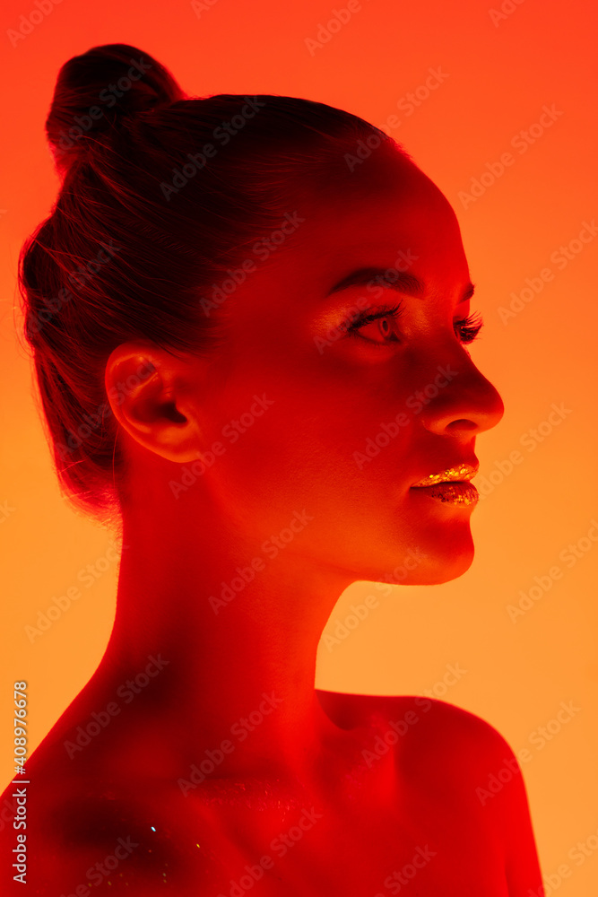 Sunset. Handsome woman's portrait isolated on orange studio background in neon light, monochrome. Beautiful female model. Concept of human emotions, facial expression, sales, ad, fashion and beauty.