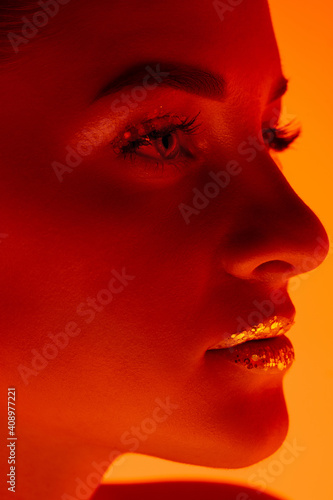 Close up. Handsome woman's portrait isolated on orange studio background in neon light, monochrome. Beautiful female model. Concept of human emotions, facial expression, sales, ad, fashion and beauty.