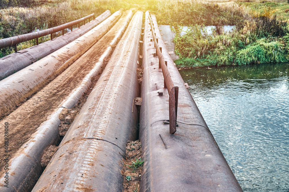Empty bridge made of old metal pipes with small railing over tranquil river at rural site in nice summer evening close view