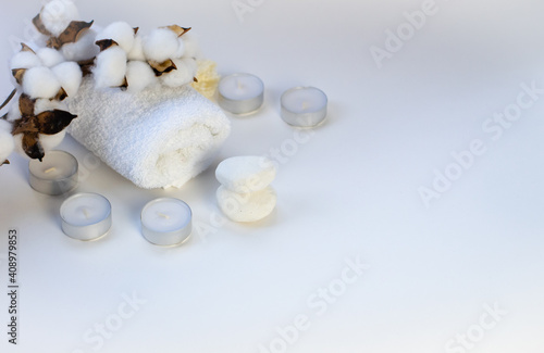 white  terry towel with a cotton branch on top and candles on a white background