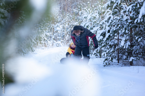 Father in winter clothes pulling sledges with his son in winter snowy forest. Happy family walk in snowy forest, outdoors © Volha Zaitsava
