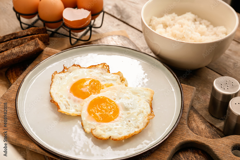 Plate with tasty eggs and rice in bowl on wooden background Plate with tasty eggs and rice in bowl on wooden background