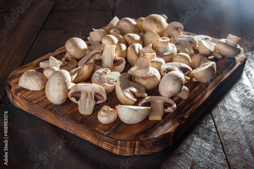 Fresh sliced mushrooms lie on a dark cutting board on a dark wooden background