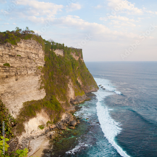 View of Uluwatu cliff with blue sea in Bali, Indonesia. Rocky cliff and sea waves at sunset.