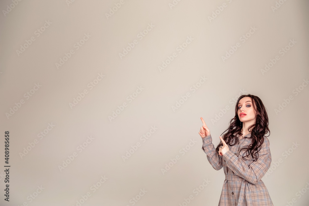 Smiling business woman pointing away while looking at the camera over gray background Smiling business woman pointing away while looking at the camera over gray background