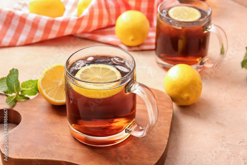 Cups of cold black tea with lemon on color background