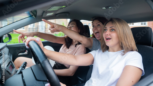 Three friends go on a trip. Caucasian women drive in a car and point fingers in surprise. © Михаил Решетников