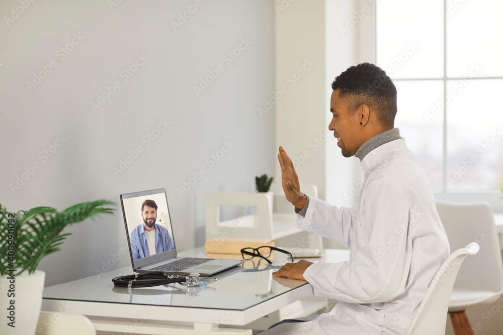 Young smiling black man doctor therapist making online consultation and greeting man patient during videocall on laptop from medical clinic office. Telehealth, telemedicine, online medicare cocnept