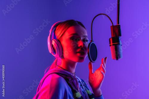 young singer in wireless headphones singing song in microphone on purple