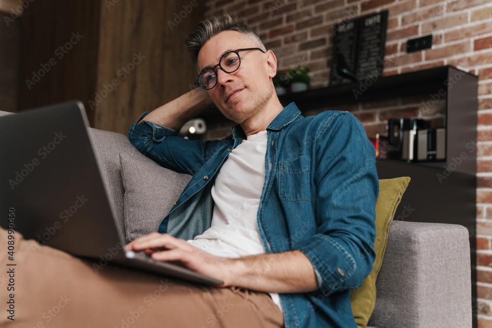 Pleased handsome man using laptop while sitting on couch Pleased handsome man using laptop while sitting on couch