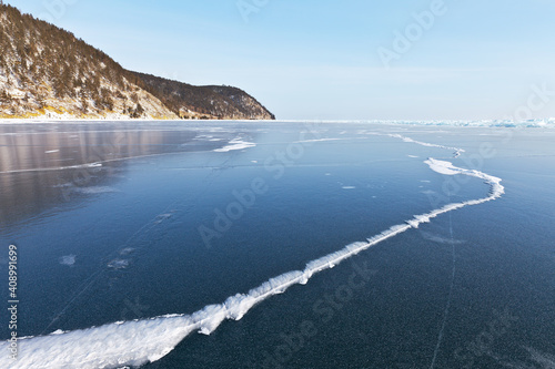Frozen Lake Baikal in January. Beautiful winter landscape with clear blue ice with crack and coastal mountains on a sunny frosty day. Natural background. Winter holidays and ice travel