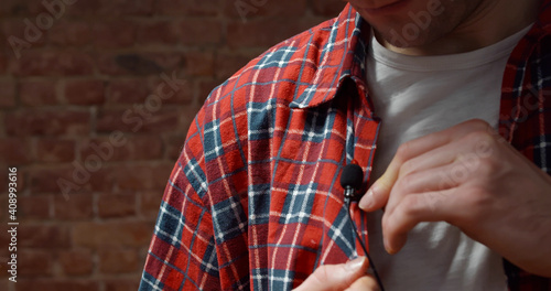 Close up of man clipping tie-clip microphone to his shirt