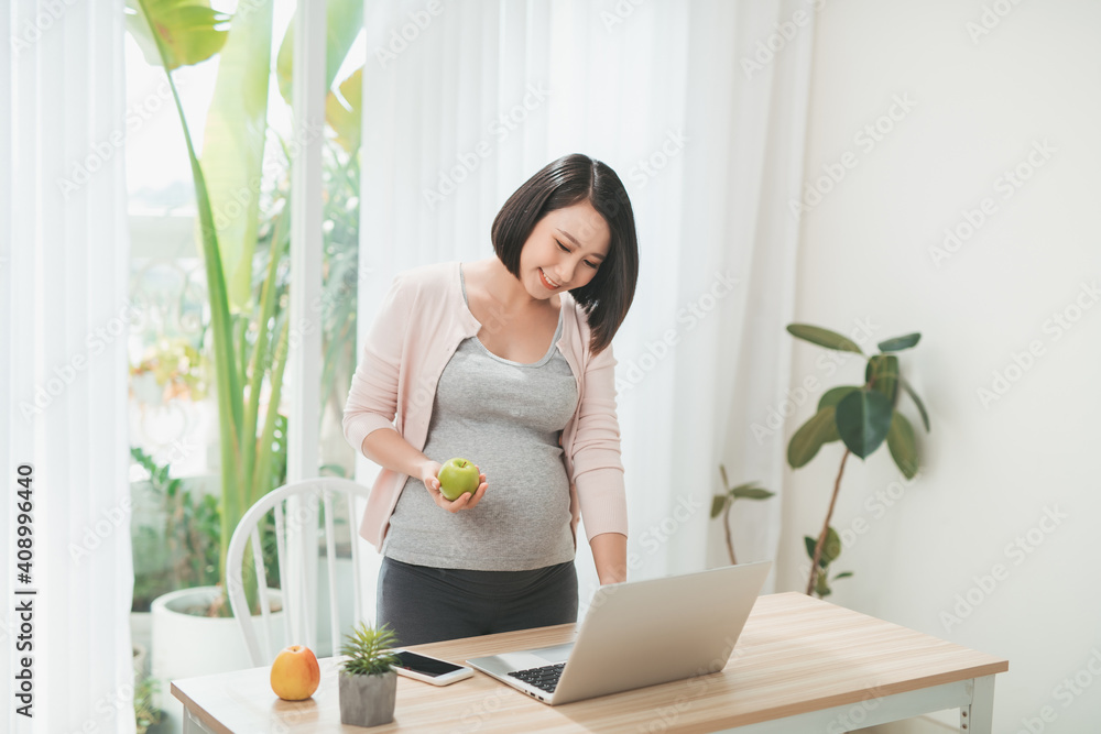 Beautiful pregnant woman with laptop and apple at home Beautiful pregnant woman with laptop and apple at home