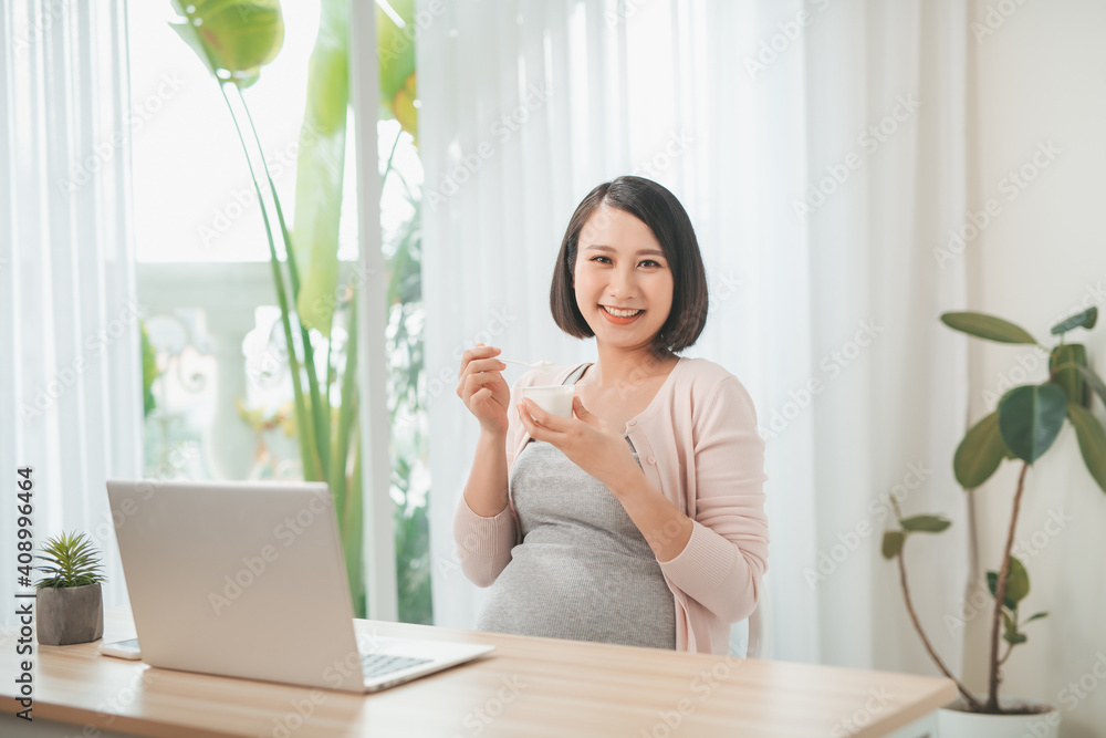 pregnancy, people and rest concept - close up of happy pregnant woman eating yogurt for breakfast at home pregnancy, people and rest concept - close up of happy pregnant woman eating yogurt for breakfast at home