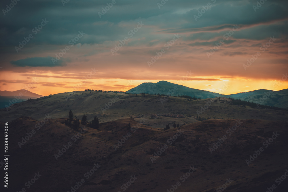 Atmospheric landscape with silhouettes of mountains with trees on background of orange dawn sky. Colorful nature scenery with sunset or sunrise. Sundown paysage in vintage colors and faded tones.