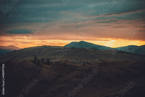 Atmospheric landscape with silhouettes of mountains with trees on background of orange dawn sky. Colorful nature scenery with sunset or sunrise. Sundown paysage in vintage colors and faded tones.