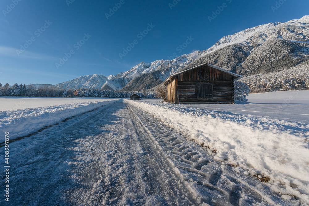 Ice covered walking path through alpine winter landscape with wooden barn in Wildermieming, Tirol, Austria
