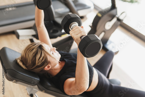 Young athletic woman doing bench press using dumbbells photo