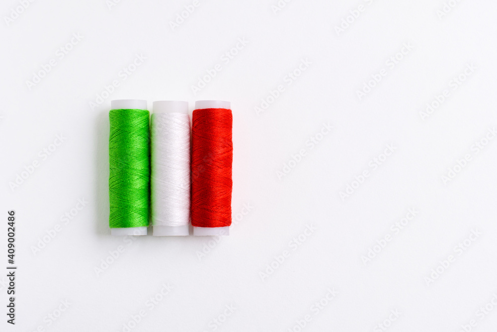 Three spools of thread for sewing are stacked in the form of the flag of Italy on a white background. Concept of Italian patriotism and the country's garment industry. There is a free empty space. Three spools of thread for sewing are stacked in the form of the flag of Italy on a white background. Concept of Italian patriotism and the country's garment industry. There is a free empty space.