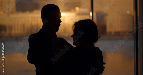 Young couple dancing and enjoying date near panoramic window with sunset cityscape