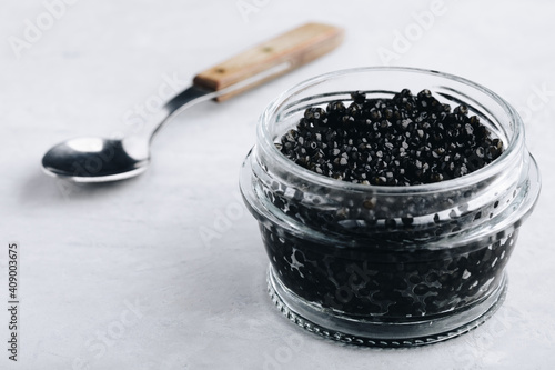 Black caviar in glass jar on white stone background,  luxurious delicacy appetizer.
