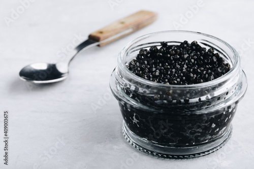 Black caviar in glass jar on white stone background, luxurious delicacy appetizer.