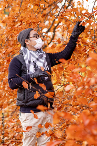 man with face mask looking at a beautiful tree outside in the cold autumn.