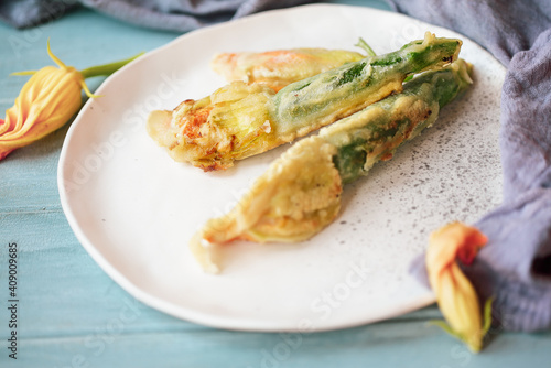 Battered and fried Courgette or Zucchini squash blossoms shot from above over a blue rustic table.