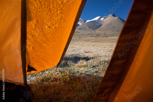 View to snow capped mountain from inside an orange camping tent.