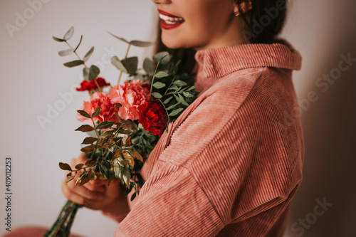 A woman in a pink sweater holding a bouquet of flowers in front of a white background. Womad day, 8 march photo