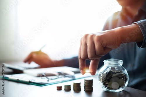 Shot of man's hand stacking coins on money stack step with glass bottle saving bank. Saving money for future plan, retirement fund with copy space. Business investment-finance accounting concept.