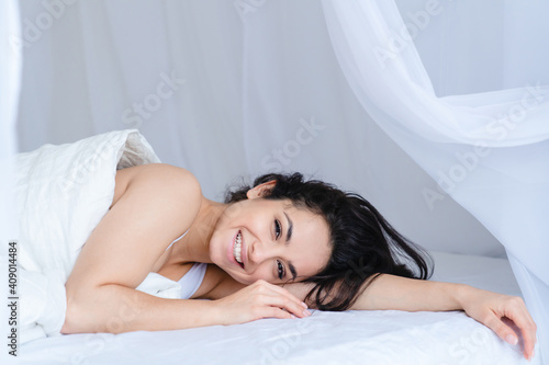 Cheerful relaxed young girl lying in the cosy white bed in the bedroom early in the morning