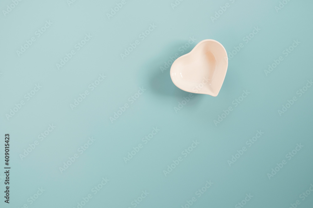 Fototapeta premium White small ceramic heart shape bowl on blue and copy space on blue background for valentines’s day concept.