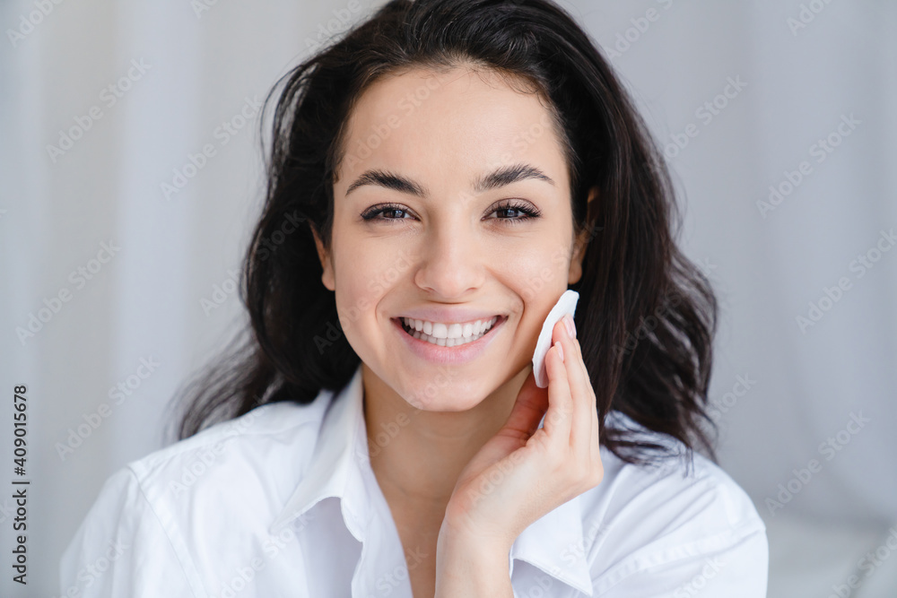 Smiling pretty young woman with clean skin using cotton pad in white comfortable bedroom Smiling pretty young woman with clean skin using cotton pad in white comfortable bedroom