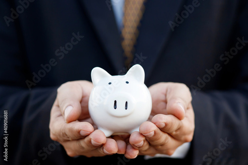 business man hold protected by hands a piggy bank on commercial. a saving money for future investment and credit financial growing concept.