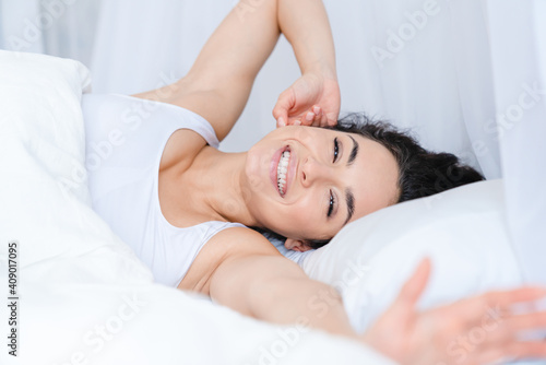 Young beautiful smiling girl stretching in her bed with white bedclothes early in the morning