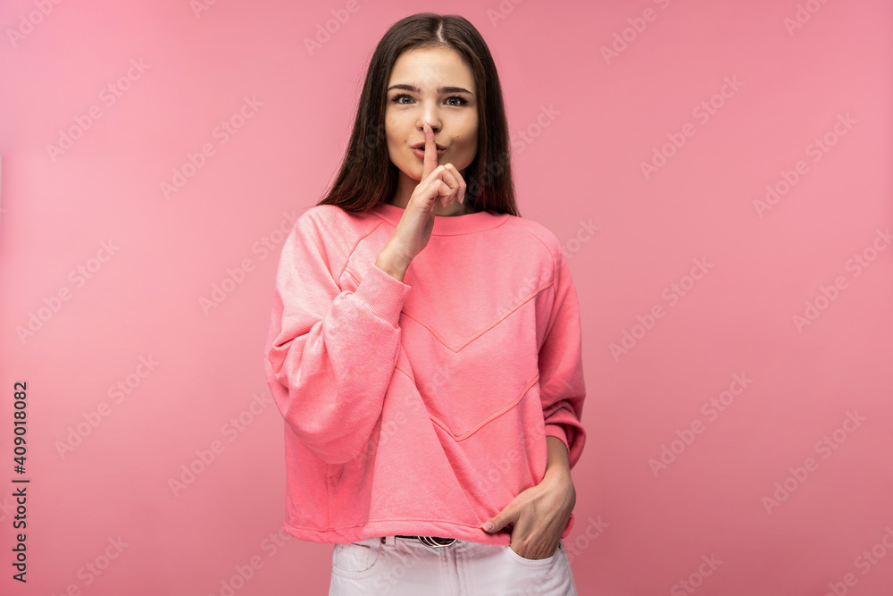 Photo of attractive young woman shows gesture not loud silence, wears casual pink t-shirt white isolated pink color background Photo of attractive young woman shows gesture not loud silence, wears casual pink t-shirt white isolated pink color background