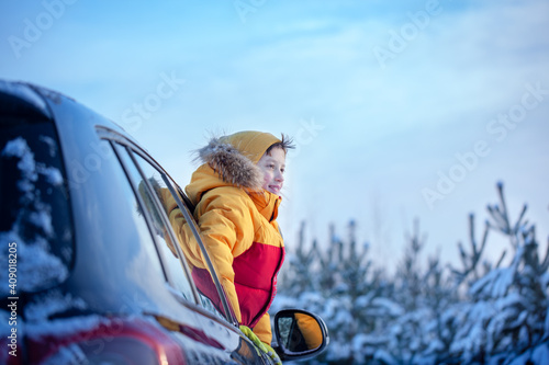 Happy little smilling boy look from a car window on a sunny day at winter snowy forest. photo