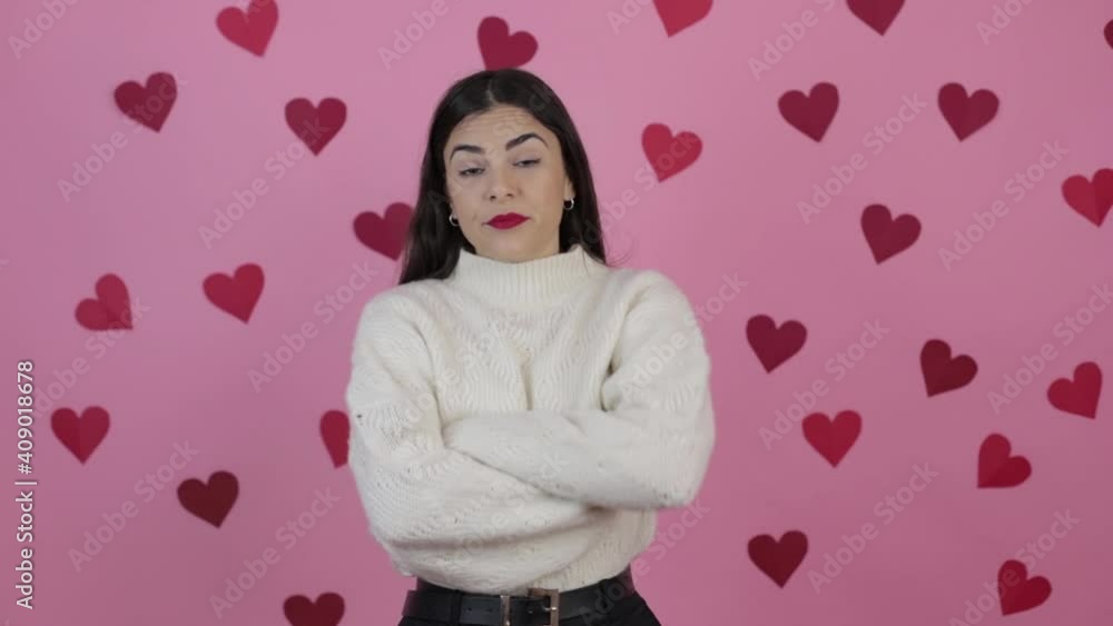 Sad beautiful woman looking at camera showing distrustful look. Studio shot on pink wall with hearts Sad beautiful woman looking at camera showing distrustful look. Studio shot on pink wall with hearts