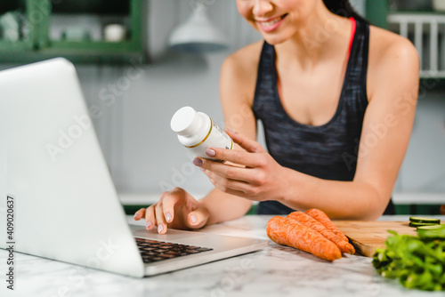 Принти на полотні Happy young woman searching info in laptop about food supplements in the kitchen