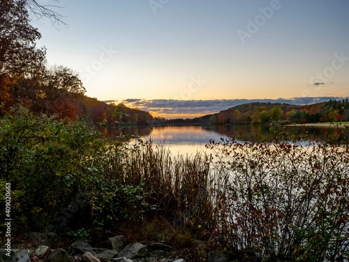 Sunset at Keystone Lake in Keystone State Park in West Moreland County in the Laurel Highlands of Pennsylvania, with the sun setting over the water, plants in the foreground and a colorful sky. photo